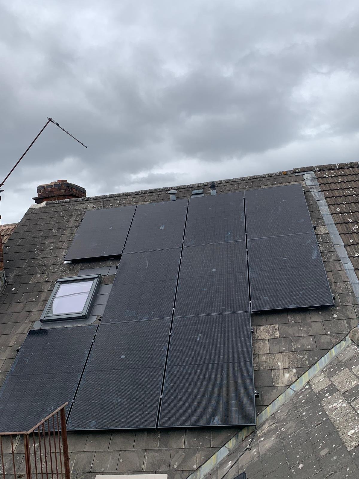 Solar panels installed beside a skylight on a weathered tiled roof
